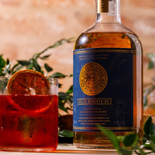 Solar Reserve Rum 55 bottle showcasing a navy and gold label design and branding, paired with a vibrant red rum cocktail.